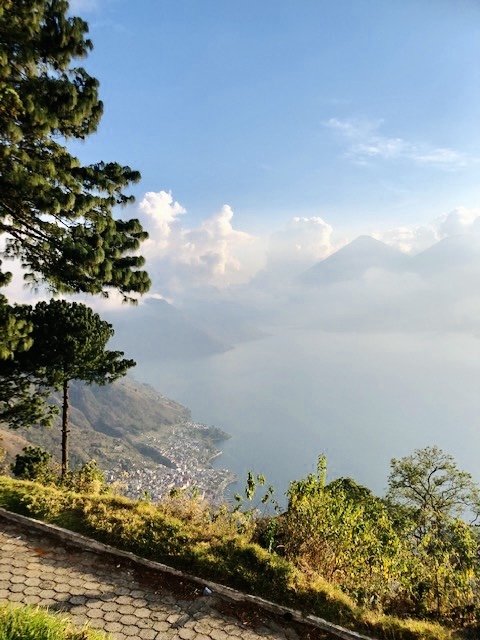A paved overlook above a lakeside town, with Lake Atitlán and volcanoes in the mist.